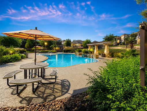 A pool area with a table and chairs and a sun umbrella.