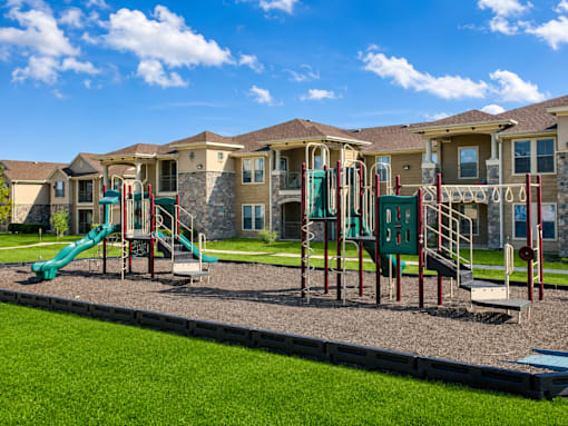 A playground with a green slide and a red and green swing set in front of apartment buildings.