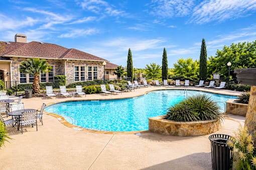 A large outdoor swimming pool surrounded by patio furniture and trees.