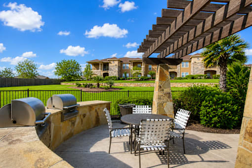 A patio with a table and chairs under a wooden pergola.
