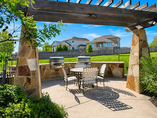 A patio with a table and chairs under a wooden pergola.