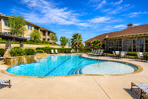 A large outdoor swimming pool surrounded by lounge chairs and palm trees.
