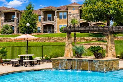 A pool with a waterfall and a bench in front of a house.