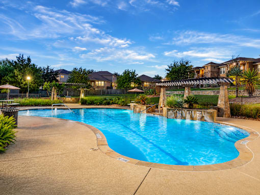 A large outdoor swimming pool with a slide and a fence surrounding the area.
