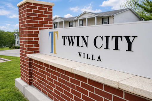 A sign that says Twin City Villa is mounted on a brick wall.