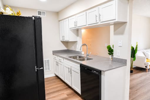 A black refrigerator stands in a kitchen with white cabinets and a black dishwasher.