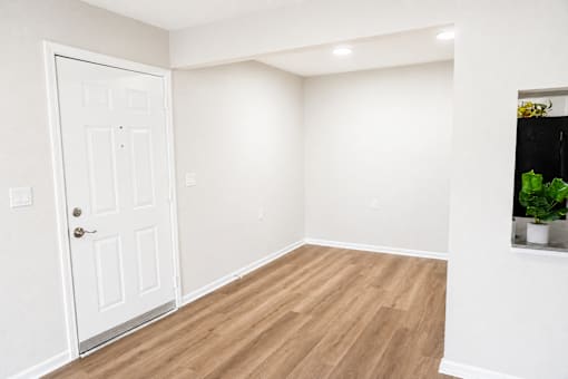 A white door is on the left of a room with wooden flooring.