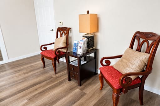 Two chairs with red cushions and a table with magazines and a lamp.