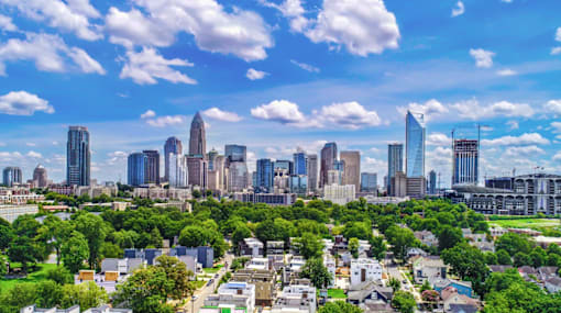 A cityscape with a mix of residential and commercial buildings, surrounded by lush greenery under a clear blue sky.