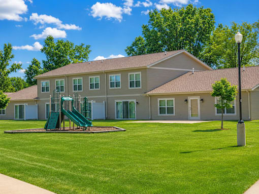 A playground with a green slide is in front of a building.