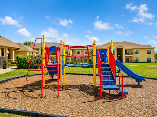 A playground with a red and yellow swing set and a blue slide.