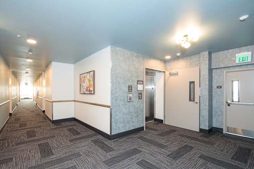 A hallway with a carpeted floor and a white wall with a picture on it.