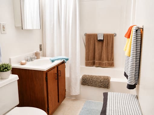 A bathroom with a white tub, a wooden cabinet, and a striped towel hanging on the rack.