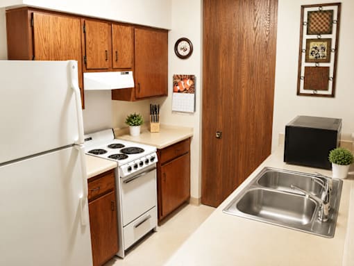 A kitchen with a white refrigerator, wooden cabinets, a stove, and a sink.