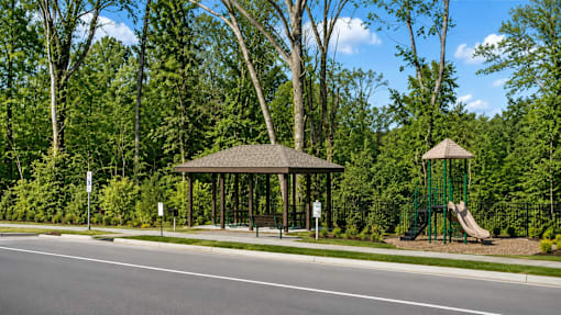A gazebo is located in a park with a playground and trees.