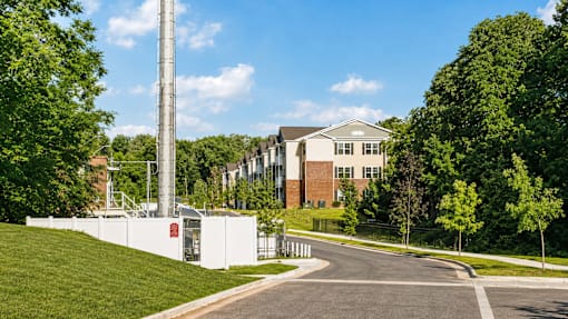 A tall white tower stands in the middle of a grassy area with trees and a building in the background.