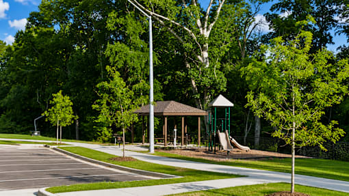 A playground with a slide and a gazebo is surrounded by trees.