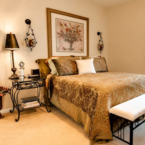 A bedroom with a bed, a nightstand with a lamp, and a framed picture on the wall.