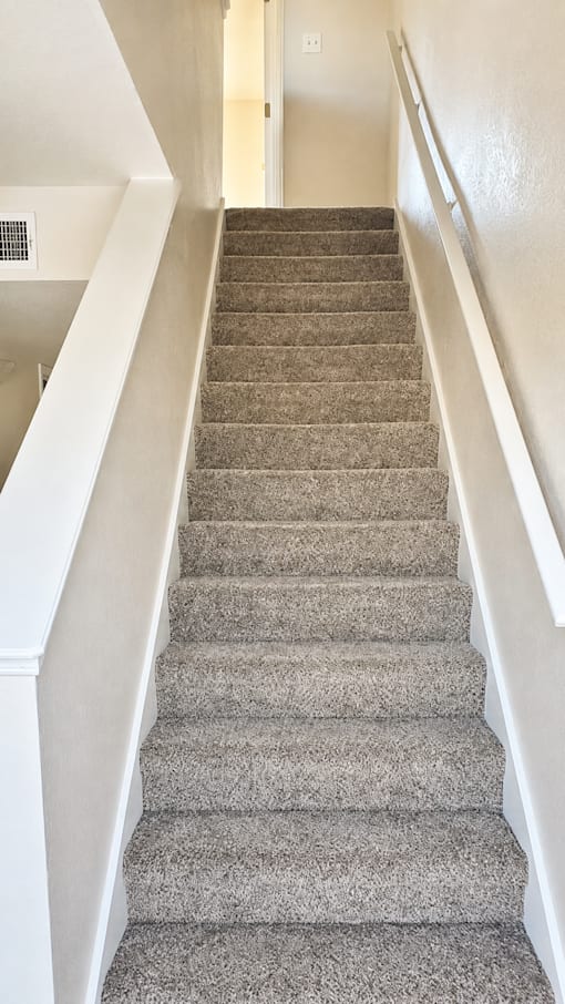 A staircase with a beige carpeted runner and white walls.