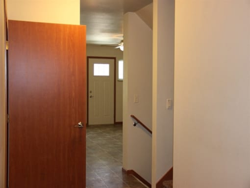 A hallway with a brown door on the left and a white door in the distance.