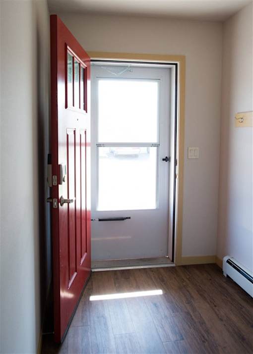 A red door is open to a room with a window.