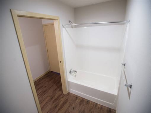 A white bathroom with a wooden door and a white bathtub.