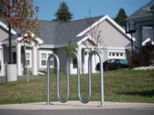 A metal bike rack sits on a sidewalk in front of a house.