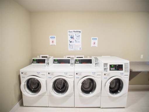 A row of white washing machines are in a room with instructions on the wall.