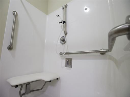 A white shower stall with a white bench and a silver grab bar.