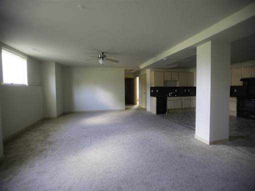 A spacious living room with a ceiling fan and a kitchen in the background.