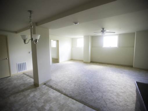 A spacious room with a carpeted floor, a ceiling fan, and a chandelier.