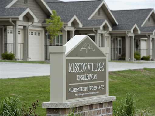 A sign for Mission Village of Sheboygan stands in front of a building.