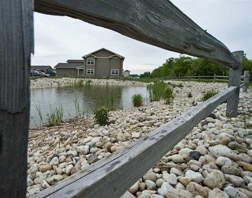 A wooden bench overlooks a pond with a house in the background.
