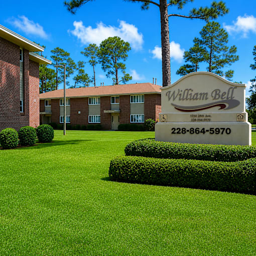A sign for William Bell stands in front of a building and trees.