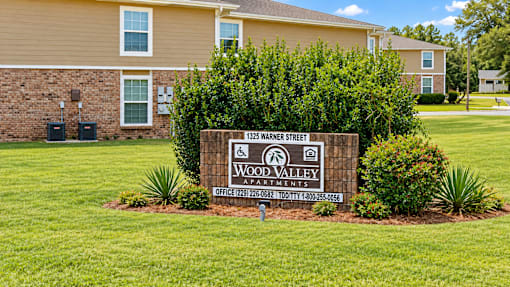 A sign for Wood Valley Apartments is in the foreground of a grassy area.