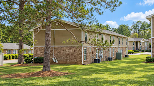 A tree stands in front of a building with a green lawn in front of it.