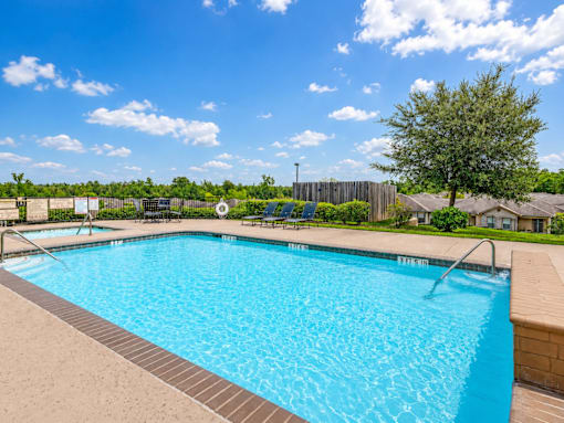 A large blue swimming pool surrounded by a fence and trees.