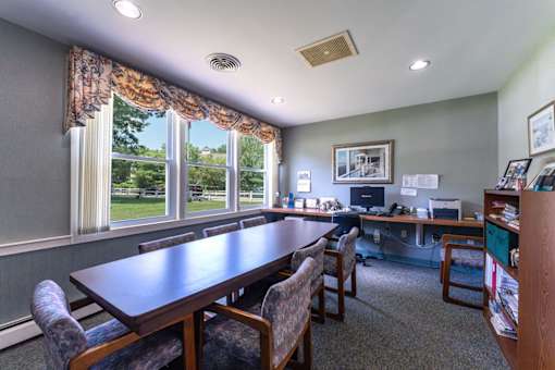 A conference room with a long table and chairs, a computer desk, and pictures on the wall.