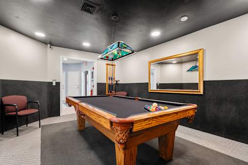 A pool table with a red chair and a mirror in a room.