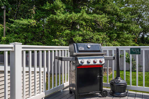 A grill is on a deck with a white fence.