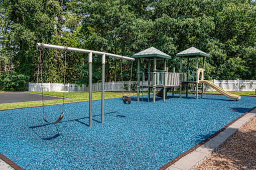 A playground with a blue rubberized surface and a swing set.