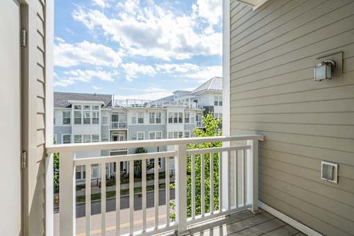 A balcony with a white railing overlooks a street with buildings in the background.