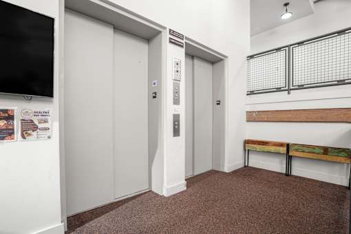 A hallway with two elevators and a bench.