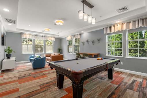 A billiard table is in the middle of a room with a blue chair and a potted plant.