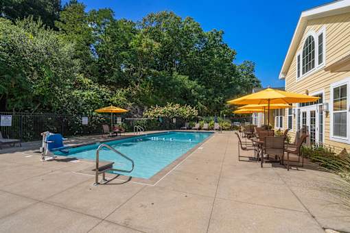 A pool area with a bench and chairs under umbrellas.