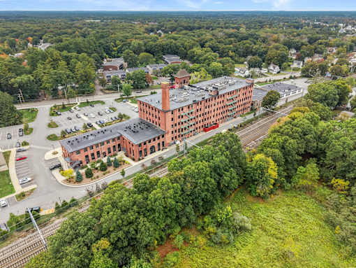 A large red brick building is surrounded by trees and a parking lot.