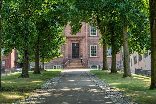 A pathway with trees on both sides leads to a building.