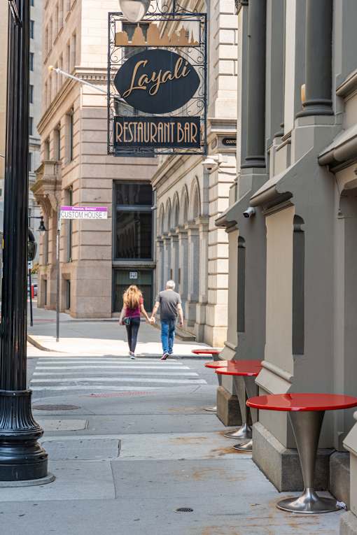 A couple walking down a sidewalk past restaurant Layali