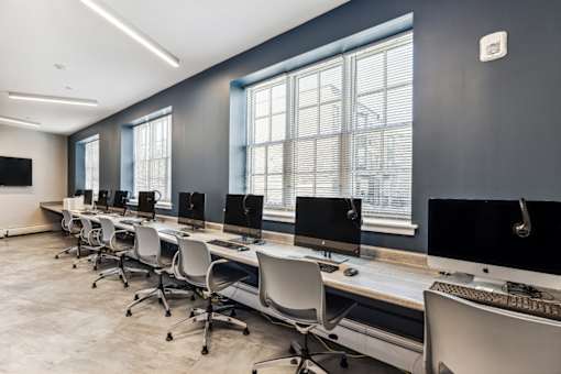 A row of white chairs are lined up in front of a row of computers.