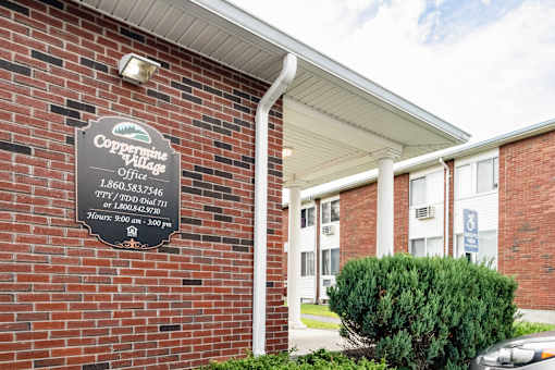 A brick building with a sign that says Coppermine Village at Coppermine Village Apartment , Bristol, CT